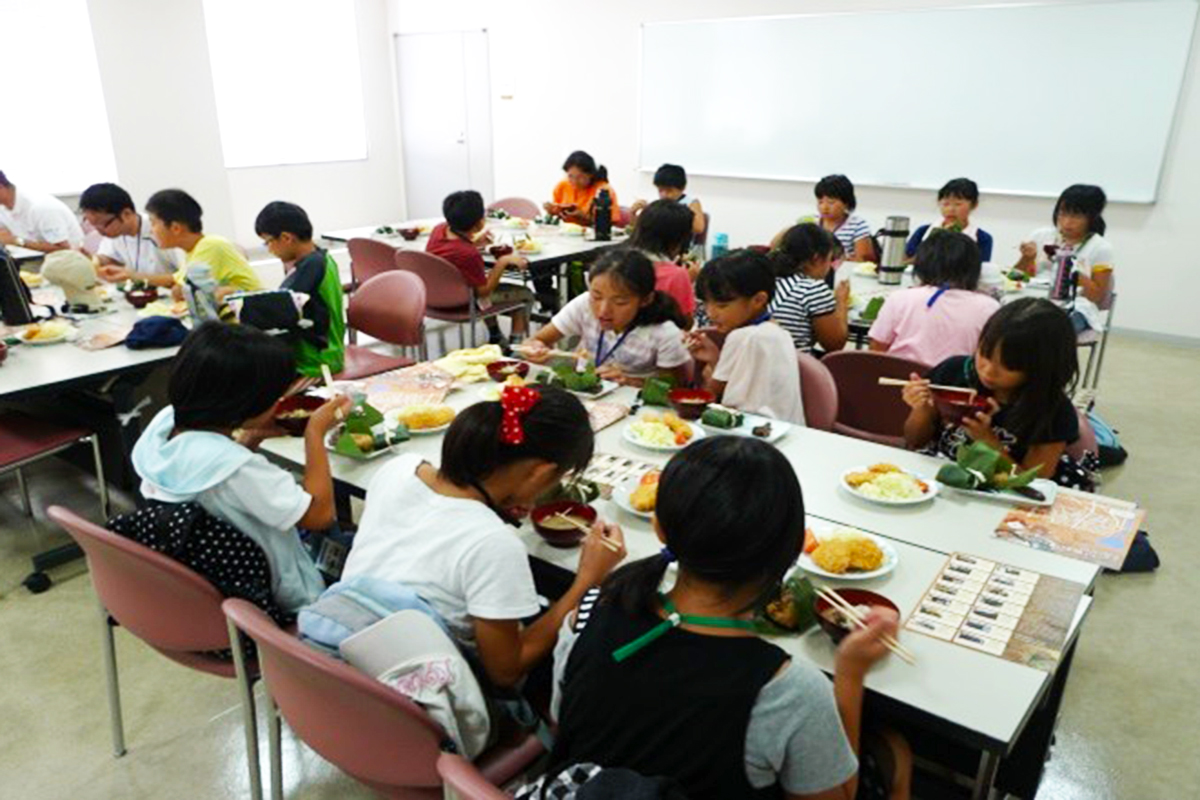 姉妹都市交流事業　川魚料理をおいしそうに食べる生徒達